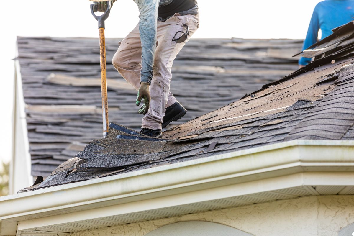 A man on a roof, diligently shoveling materials, with a bright sky in the background.