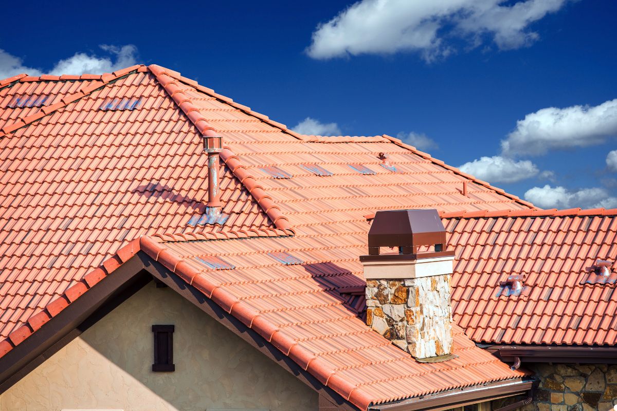 A charming house with a red tile roof and a prominent chimney, surrounded by greenery. 