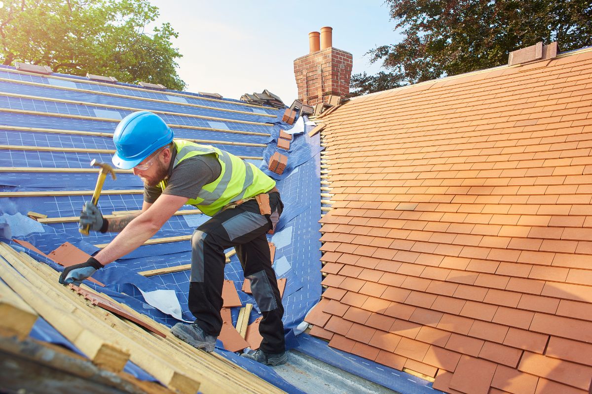 A roofing professional in a hard hat and safety vest, focused on a roof replacement, emphasizing safety and expertise.