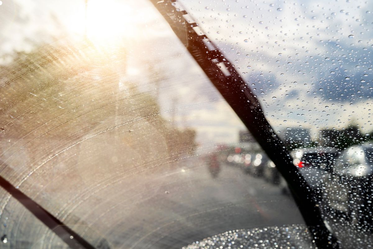 A car windshield displaying numerous raindrops, distorting the view beyond and emphasizing the rainy weather.